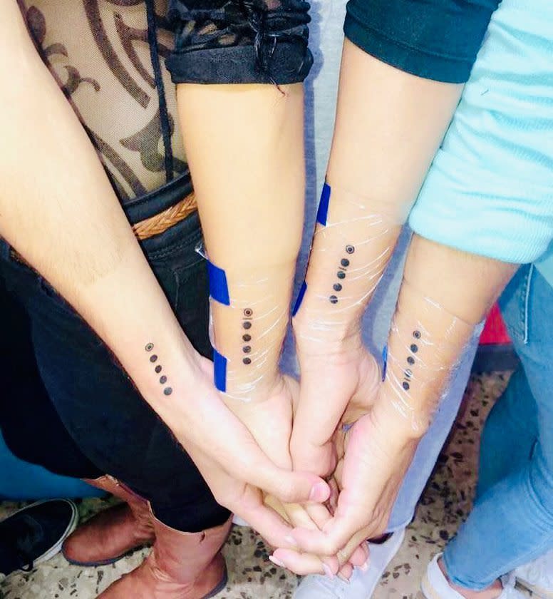 Three forearms with vertical rows of black dot tattoos wrapped in plastic